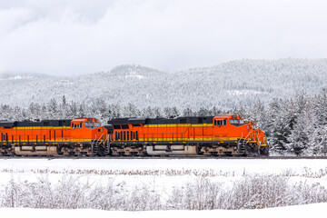 two freight trains, with three locomotives visible, pulling cargo through a mountainous region...