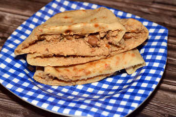 A flat bread with mashed fava beans mixed with oil, sesame tahini, cumin, spices, slices of chili...