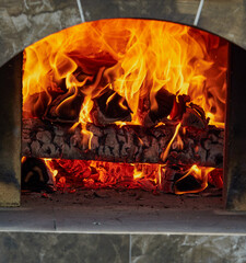 Burning firewood in fire-box of fireplace in country cottage. Rustic cooking oven with burning logs.