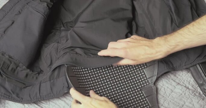 Hands place the plastic motorcycle back protector inside the motorcycle jacket. Fasten the zipper. Preparing for a motorcycle trip, protection.