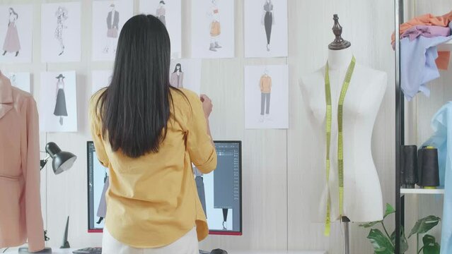 Back View Of A Female Designer With Sewing Machine Putting A Picture On The Wall While Designing Clothes In The Studio
