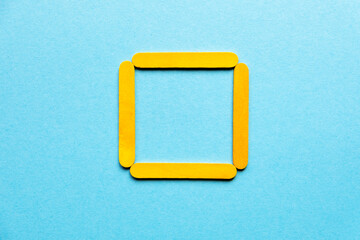 yellow square made of wooden sticks on a blue background. Geometric figure. Hobbies for children. Wooden sticks for construction