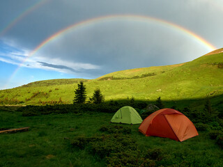 A tourist tent in the mountains on the background of a rainbow.