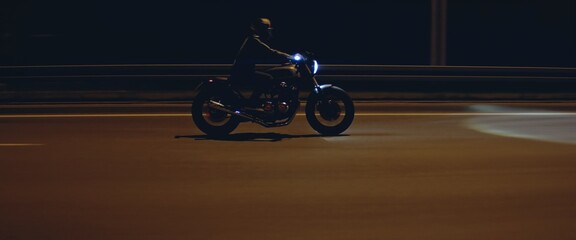 Biker riding his custom built cafe racer motorcycle through city at night. Shot with 2x anamorphic...