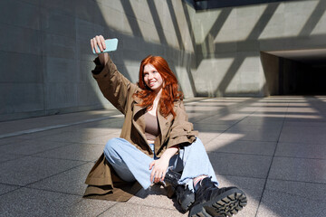 Happy redhead teenage girl user hipster using smartphone talking selfie or having video chat...