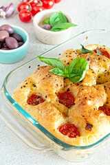 Fresh Italian flat bread Focaccia with tomatoes, olives, garlic and herbs on a light background.