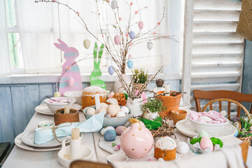 Table decoration for Easter celebration in kitchen.Tablescape for Easter holiday at home.Family religious traditional festive christianity,catholic meal food.Pop color eggs,cake,fun bunny,candy sweet