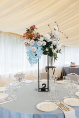 Wedding ceremony area in a marquee. Round tables for dinner. composition of artificial flowers on the celebration. wedding decor in blue and pink tones in nature. 