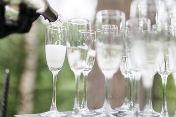 Bartender pouring champagne or wine into wine glasses on the table at the outdoors solemn wedding ceremony. 