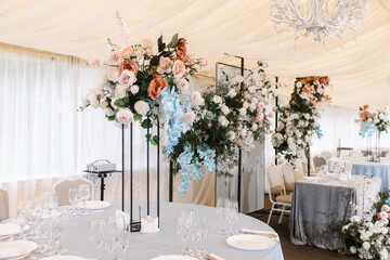 Wedding ceremony area in a marquee. Round tables for dinner. composition of artificial flowers on the celebration. wedding decor in blue and pink tones in nature. 