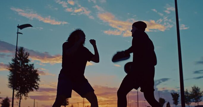 silhouettes of black fighter and his coach during outdoor workout in sunset time, 4K, Prores