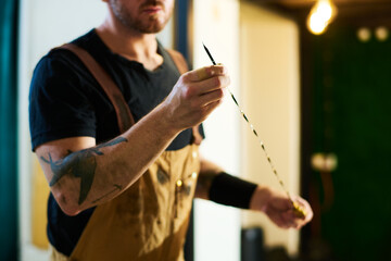 Young technician in apron holding sharp metallic wire while preparing work instrument for check up of engine of broken car
