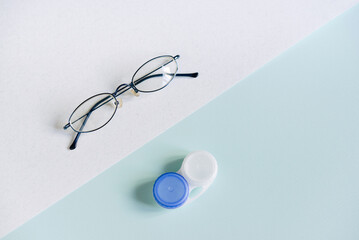 Glasses and a case for contact lenses on a white and blue background. concept of choosing a method...