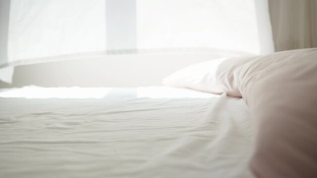 It's a sunny morning, the light from the window falls on the white bed, the wind blows the curtains. Dolly slider close-up.