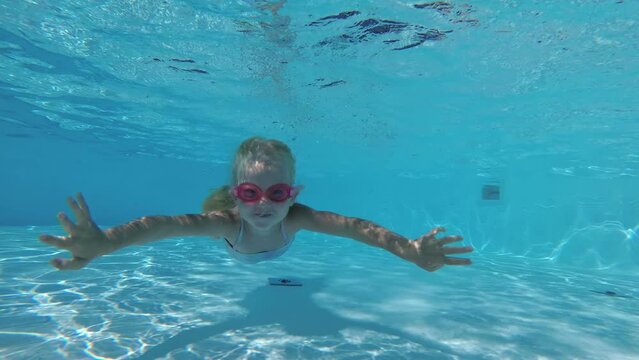 Girl child 5 years old swims underwater in an outdoor swimming pool