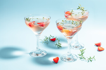 Glass of strawberry cocktail or mocktail, refreshing summer drink with champagne, strawberries, ice cubes and rosemary on blue background