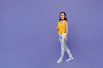 Fototapeta na wymiar Full body side view young happy fun woman 20s she wear yellow tank shirt look camera walking going strolling isolated on plain pastel light purple background studio portrait. People lifestyle concept.