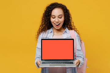 Naklejka premium Young black teen girl student she wear casual clothes backpack bag hold laptop pc computer blank screen workspace area isolated on plain yellow color background High school university college concept.