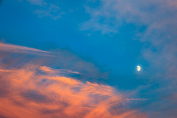 Colorful evening sky over Europe, red evening sun on blue summer sky and already visible moon. Sight for dreaming or as a beautiful background. 