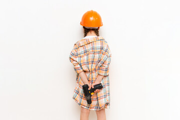 The child holds a screwdriver on his back. A cordless drill in your hands. The concept of...