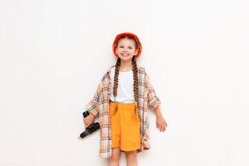 A child in a construction helmet and with a drill in his hands on a white isolated background. A little girl with long pigtails is getting ready for renovation in the nursery.