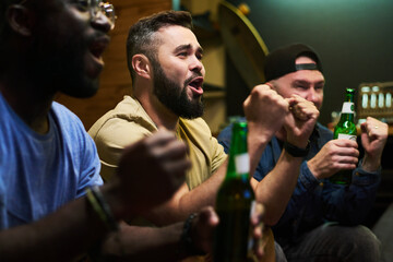 Group of football fans expressing joy and shouting excitedly while watching broadcast of match of...