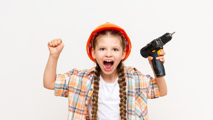 A little girl holds a drill and screams. A child in a construction helmet on a white isolated...