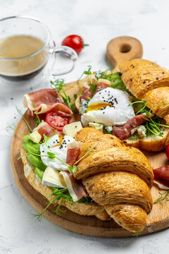 Spanish breakfast, Croissant Toast or sandwich with Poached egg, jamon, blue, cheese, avocado, microgin and cherry tomatoes, Cup of coffee, Food recipe background. vertical image