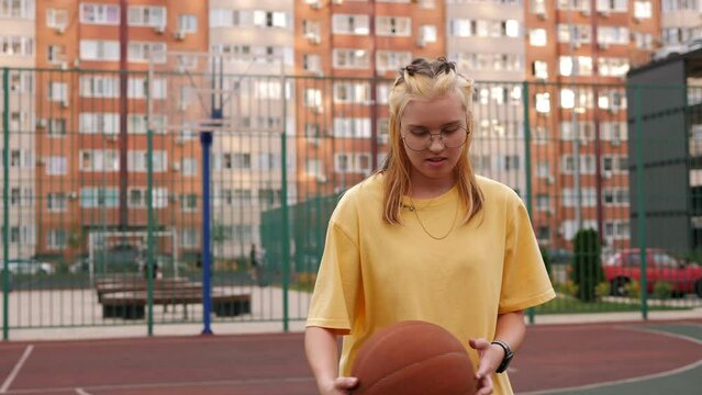 A teenage girl with a basketball in her hands on the court in the courtyard.