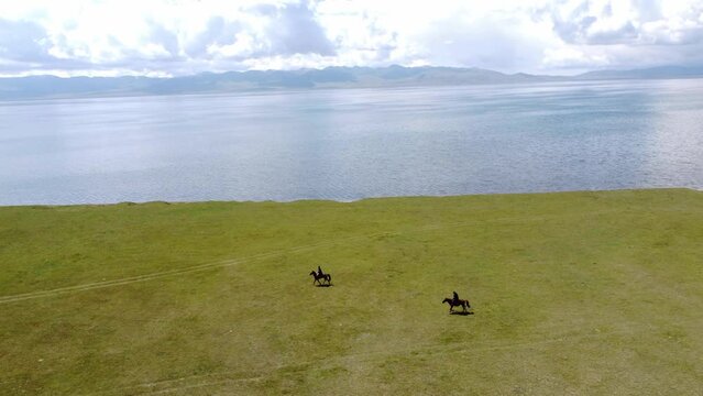 Mans ride on horses near to Song-Kul lake in Kyrgyzstan. Drone footage 4K.