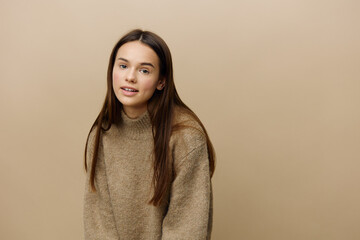 a sweet, modest, sophisticated woman stands on a beige background in a textured, warm sweater and...