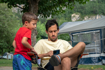 Obraz premium young man with a kid sitting at a campsite using a mobile phone