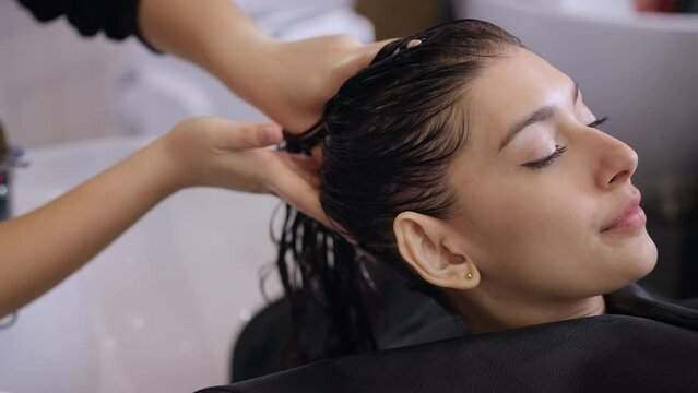 Caucasian young woman get hair washed by hairdresser stylist in salon. Beautiful customer girl lying down on salon washing bed feeling relax and happy enjoy massaging her head at beauty barber shop.