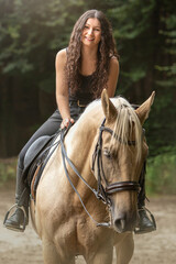 Portrait of a young woman riding a palomino kinsky warmblood horse in summer outdoors. Equestrian riding scene