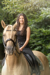Portrait of a young woman riding a palomino kinsky warmblood horse in summer outdoors. Equestrian...