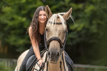 Foto op Canvas Portrait of a young woman riding a palomino kinsky warmblood horse in summer outdoors. Equestrian riding scene © Annabell Gsödl