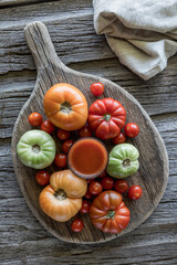 A glass of fresh tomato juice surrounded by tomatoes on a rustic board.