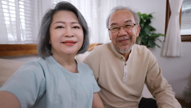 Asian elderly couple woman and man using mobile phone talking at home. Mature older grandmother and grandfather use smartphone video call with son, daughter feeling happy with communicate via internet