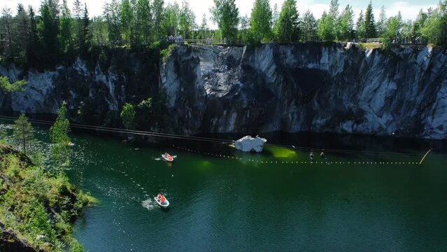 Concept of traveling in Russia. Republic Karelia June 2022. Tourists on rowing boat. Ruskeala Mountain Park is popular tourist destination. Beautiful natural marble wall and turquoise lake.