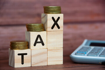 Tax word on wooden blocks with gold coins on top and calculator background. Tax concept
