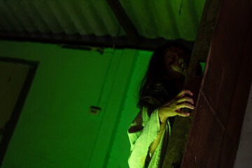 The green light shows the face of a female zombie in a bloody abandoned house for Halloween.