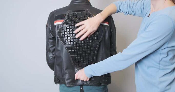 A woman applies a back protector to a leather motorcycle sport jacket worn by a biker. Moto accessories, saving the life of a motorcyclist. Fitting protection, rear view, close-up.