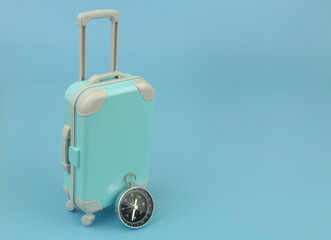 Compass and mini suitcase on blue background with copy space for text. 