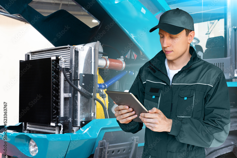 Aufkleber Serviceman with digital tablet on a background of the tractor with open hood