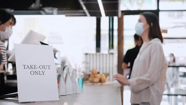 Asian woman customer wearing mask receive drink on coffee bar counter. Attractive young female consumer wear face mask due covid-19 pandemic, get food bag take away from barista worker in coffee shop.