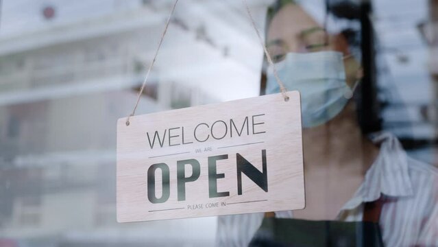 Caucasian beautiful waitress wear mask, turns open sign on glass door. Attractive Coffee shop owner prepare to welcome customer to reopen small business after COVID-19 ended lockdown and quarantine.