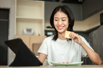 Woman is having breakfast with crackers mixed with various grains and using tablets to update her morning news, Small room in condominium background, Wake-up activities