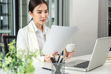Professional businesswoman analyzing graph data from document in hand, Market research reports and income statistics, Woman working in a private office, Financial and Accounting concept
