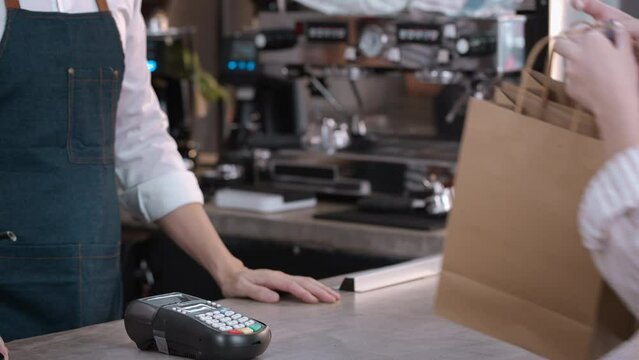 Close up hands of woman use credit card to pay for takeaway in cafe. Restaurant worker giving takeaway food bag to Young girl customer after order and make a quick contactless payment in coffeehouse.
