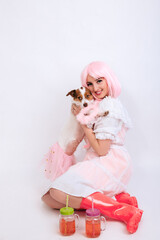 A girl with pink hair, in a vintage white dress and pink rubber boots sits and hugs her dog in a pink outfit on a white background isolated on a white background. 